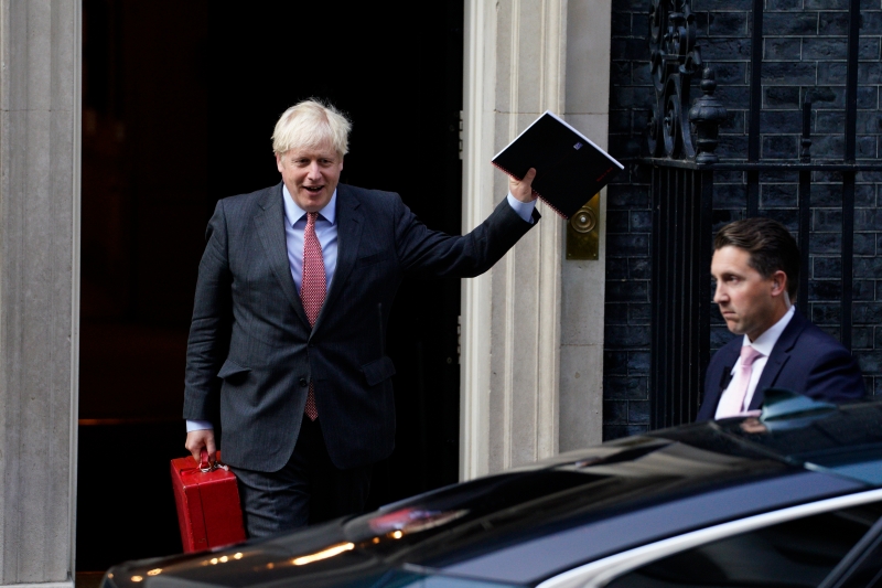 英国首相约翰逊周一离开唐宁街10号时挥手致意。BBC报道，约翰逊料会宣布上调英国疫情警戒，以遏制冠病病毒扩散。（欧新社照片）