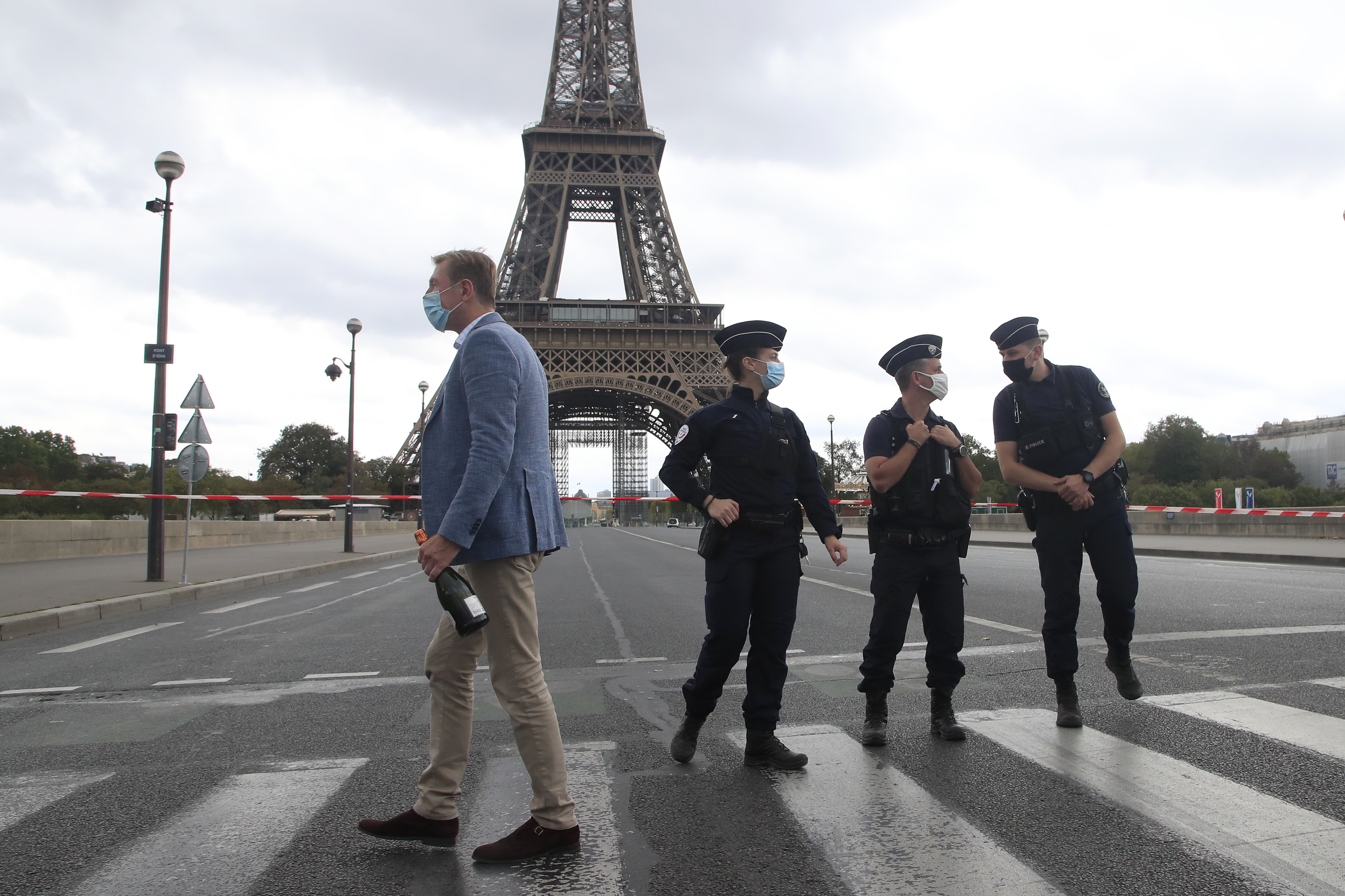 警方接获投报后赶往现场封锁埃菲尔铁塔，一名俄罗斯游客手里拿着一瓶香槟路过现场。（美联社照片）