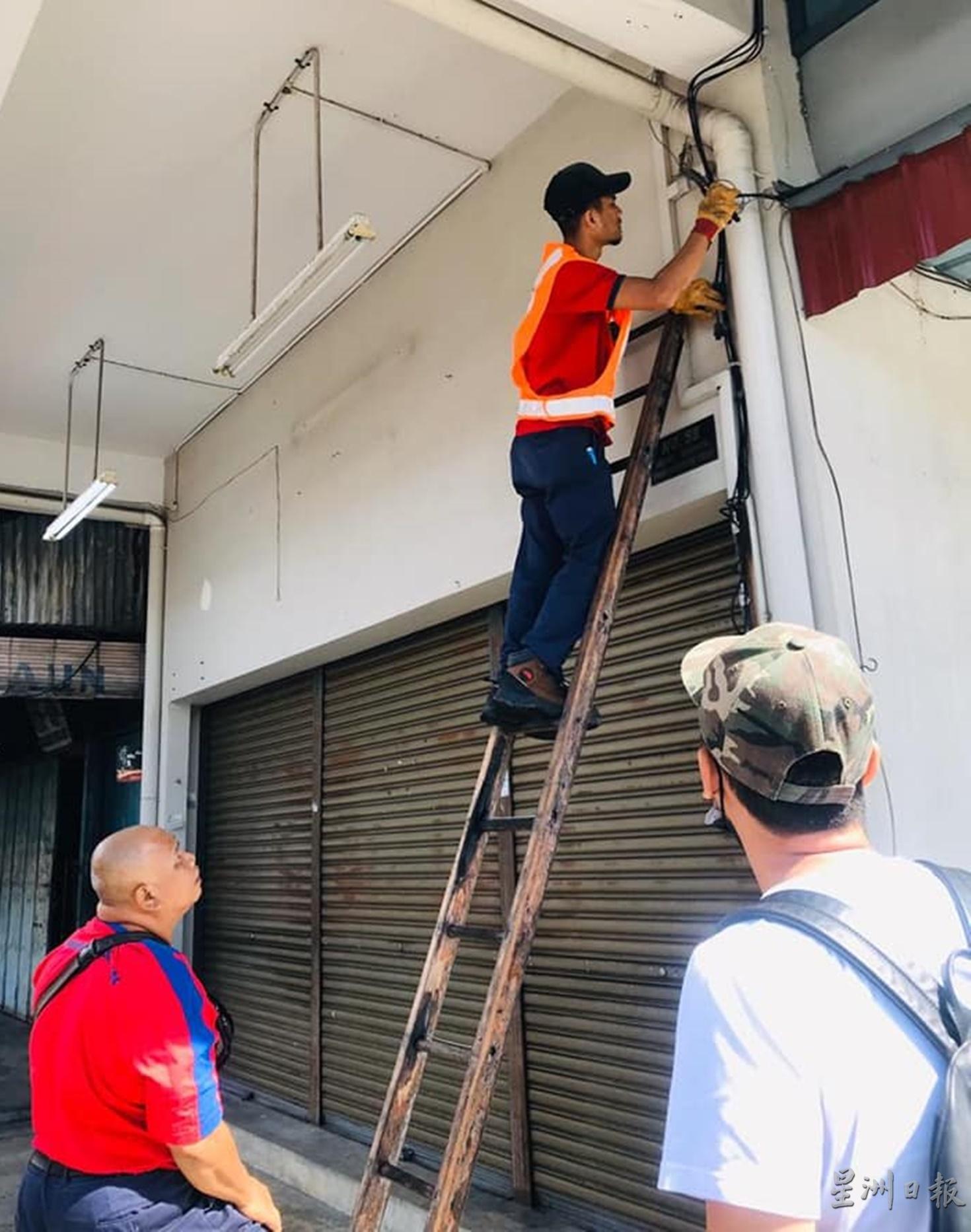 国能公司技工登上梯子，将衔接到商店内的电线剪断。
