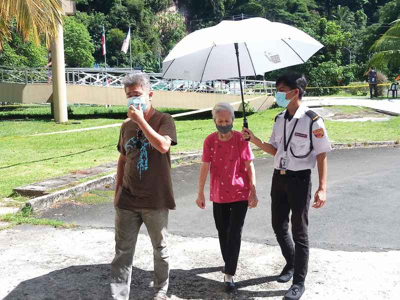 工作人员为步行前往投票站的长者撑伞。