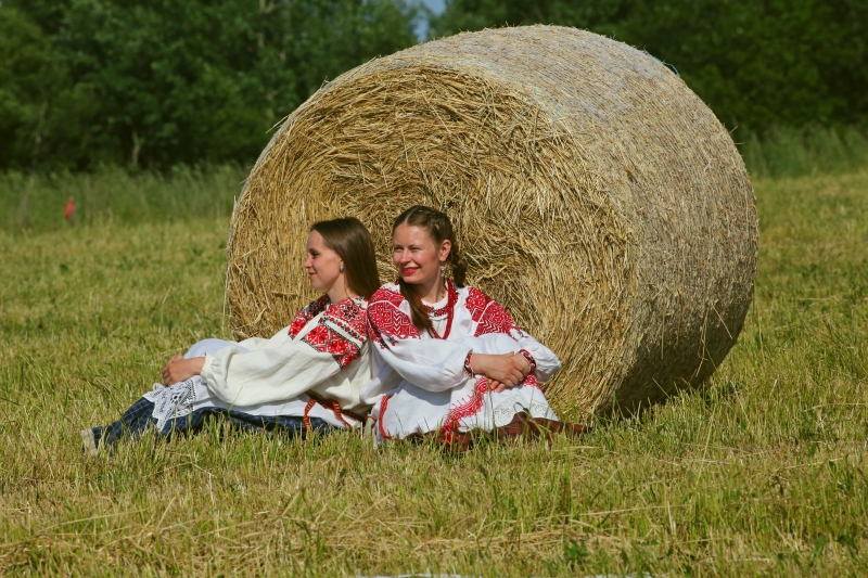 两位身著民族服装的姑娘坐在乾草捆边拍照打卡。　