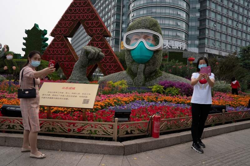 两名戴着口罩的女子周一在北京一个向对抗冠病的医务人员致敬的大型装饰物前自拍。（美联社照片）
