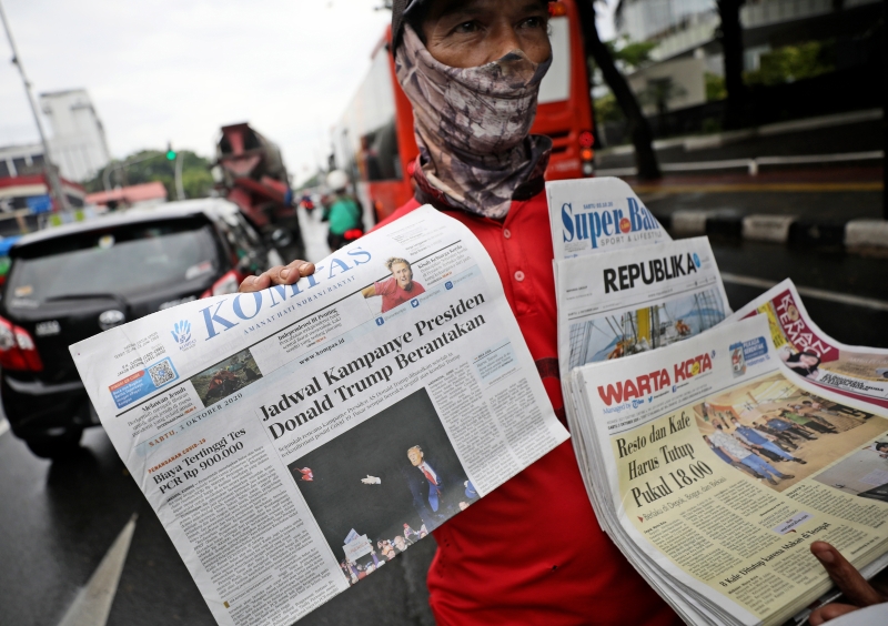 在印尼雅加达街头，一名报贩手上的报章在封面报道了特朗普染病的消息。（美联社照片）