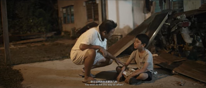 《无私》的阿山（左）见少年在废弃院子中阅读，发现他无父无母，当下决定收养少年给他一个家。这是一个讲述马来西亚种族和谐的故事。（截图自影片）