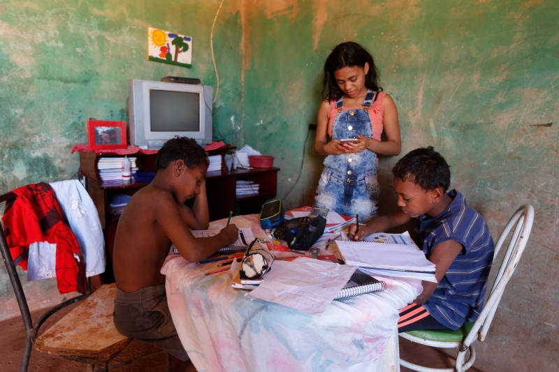 巴西首都巴西利亚圣卢西亚街区一户贫困家庭的姐姐辅导两个弟弟上网课。（新华社照片）