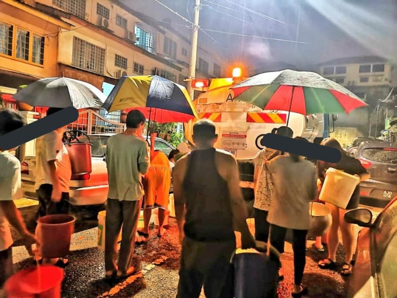 居民在雨天排队取水时，一手撑伞，一手提着水桶。