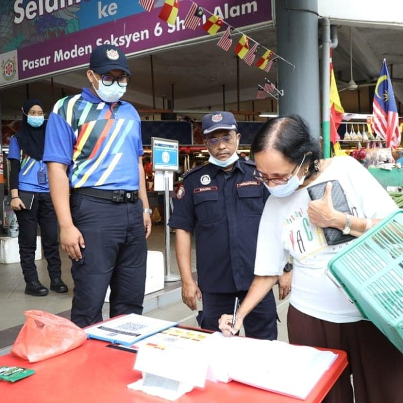 市政厅执照组官员和执法人员在沙亚南第6区巴刹驻守，确保公众有扫码签到或手写登记，贯彻防疫守则。