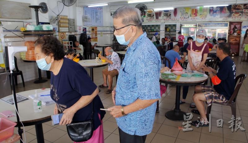 顾客排队使用红外线体温测量仪测量体温是现在的新常态。