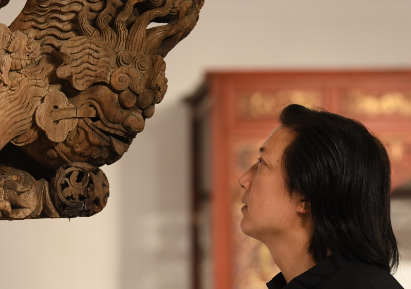 浙江省工艺美术大师陈国华在工作室观察收藏的老木雕建筑构件的细节 。

