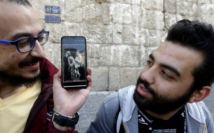 Bader holds up a black and white photo showing two men, one blind and carrying a friend who could see but not walk. AFP