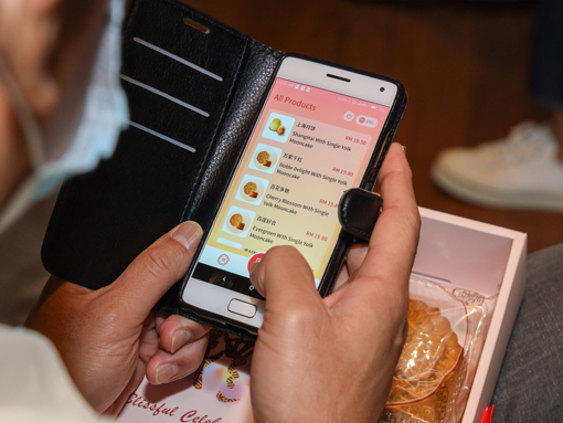 一名顾客正使用“TraX”手机应用程式扫描海外天月饼包装上的二维码，仔细浏览月饼的信息。