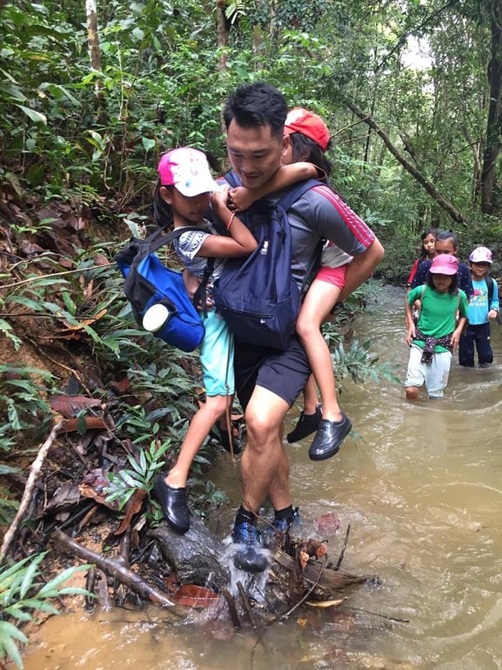 一名青年又背又抱，协助两名幼童渡河。