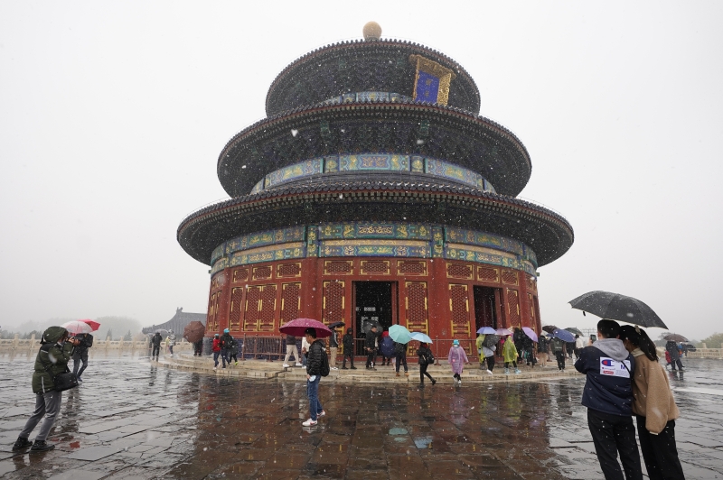 游客撑着雨伞在北京天坛公园赏雪游览。

