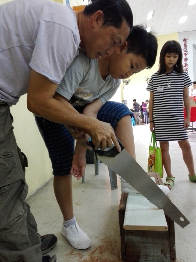 薛应杰在小木凳亲子工坊里让孩子决定木凳子该多高多长，大人则协助锯木、钉钉子的操作。