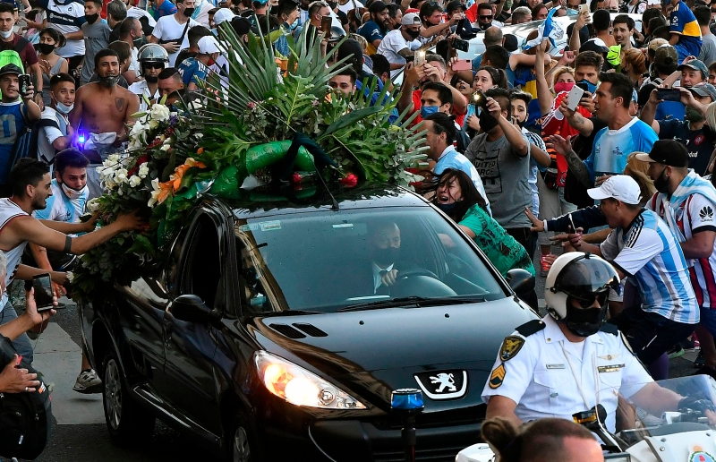 一位工作人员驾车把马拉多纳遗体护送去公墓途中被路旁激动的民众又抓又拉，场面失控。（法新社照片）

