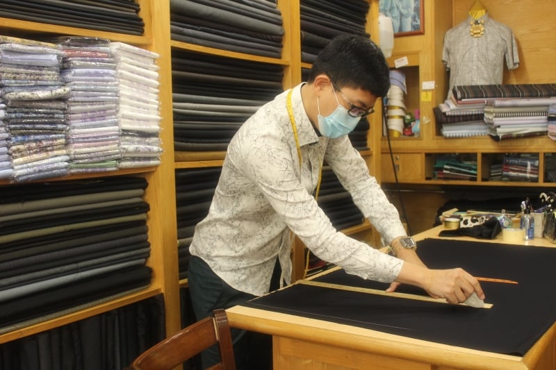 高登服装第二代接班人刘征槟为西装布料画版型，再送到裁缝代工处帮忙缝制成衣。