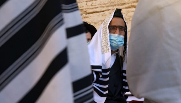A young Ultra-Orthodox Jewish man wears a face mask and a tefillin during prayers at the Western Wall in the Old City of Jerusalem. AFP