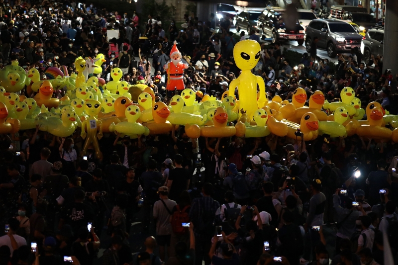 泰国反政府示威者高举一群充气小黄鸭，小黄鸭曾于本月17日被用来抵挡警察水炮的黄色小鸭，成为民众争相合照的吉祥物。因为黄色小鸭圆胖、微笑、无害的形象，有不畏强权的意思，因此被当成吉祥物。（法新社照片）