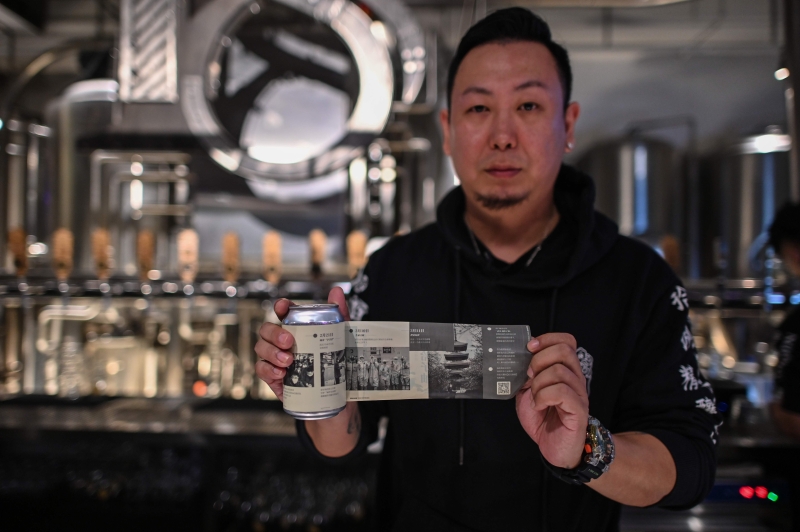 中国武汉一家叫18号酒馆的老板王帆展示其酒厂为记念76天武汉封城的艰难岁月而推出的一款内藏“乾坤”的啤酒“武汉加哈子油”。（法新社照片）