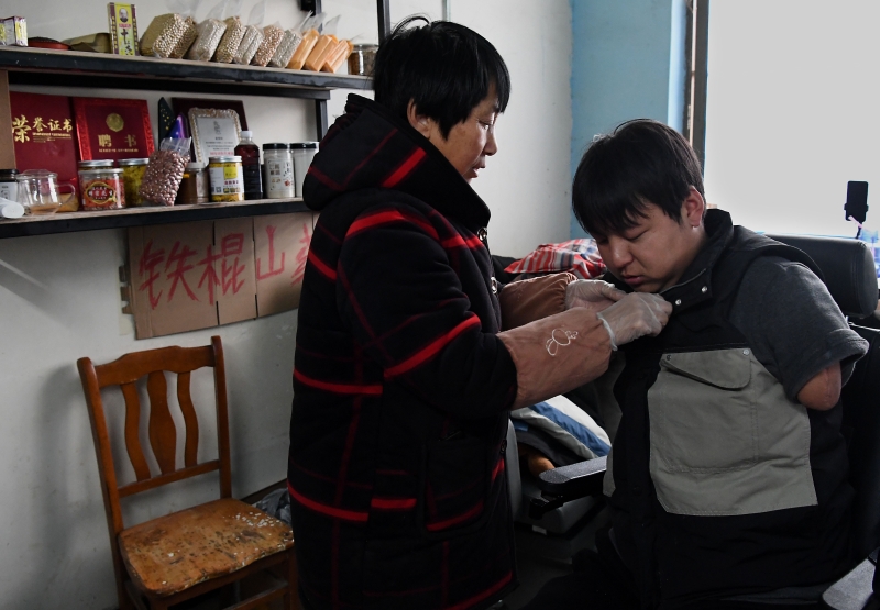 在孙亚辉出门直播前，母亲（左）帮他穿衣。 （图：新华社） 