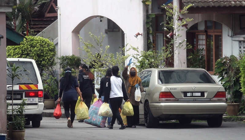 居民从保安亭接过采购的物品后，提着大包小包的日用品返回住处。