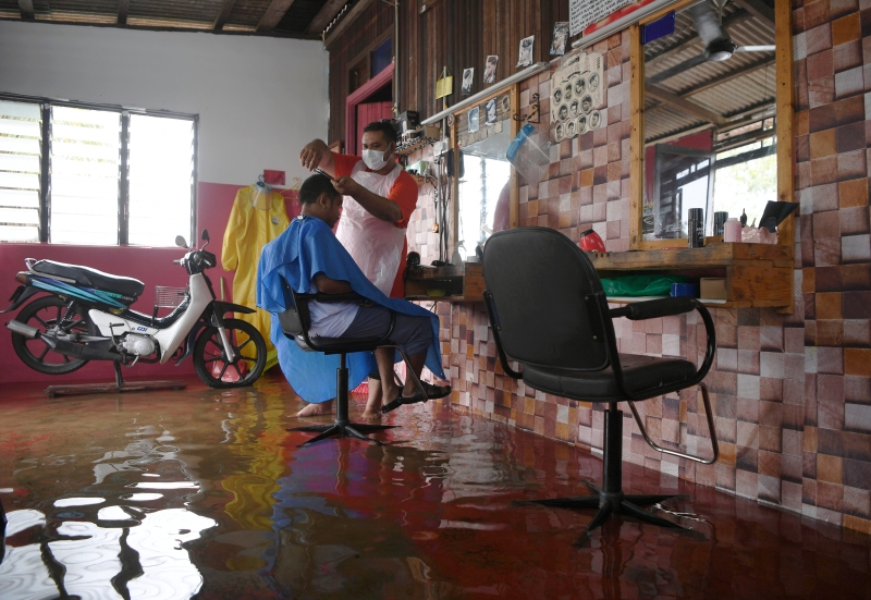 莫哈末扎夫仁（站者）站在水中为顾客阿沙鲁丁理发。(图：马新社）