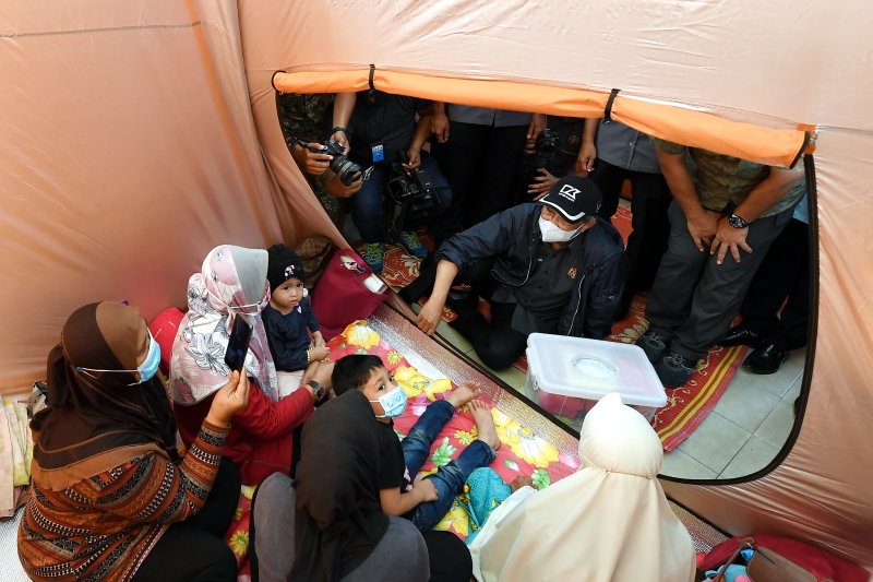 首相走访甘马挽灾区时时派发物资予住在疏散中心的灾黎，同时提醒众人遵守标准作业程序，小心防疫。