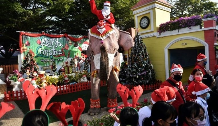 An elephant from the Ayutthaya Elephant Palace dressed in a Santa Claus costume and wearing a face mask, is greeted by students during an event to hand out masks at a school in Ayutthaya. AFP