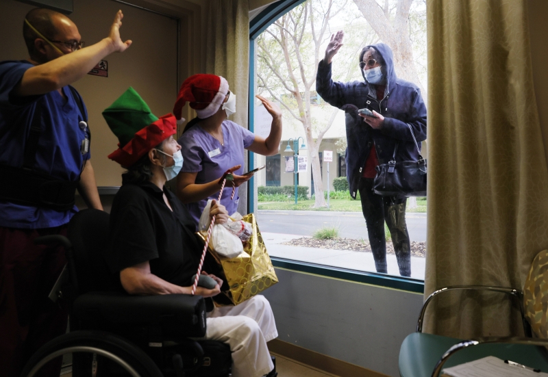 圣诞节当日，美国加利福尼州米申希尔一所疗养院的院友却只能在护理员陪伴下，隔窗向院外该院友的亲人挥手和通过手机对谈。碍于疫情，许多医护设施谢绝探访。（法新社照片）


