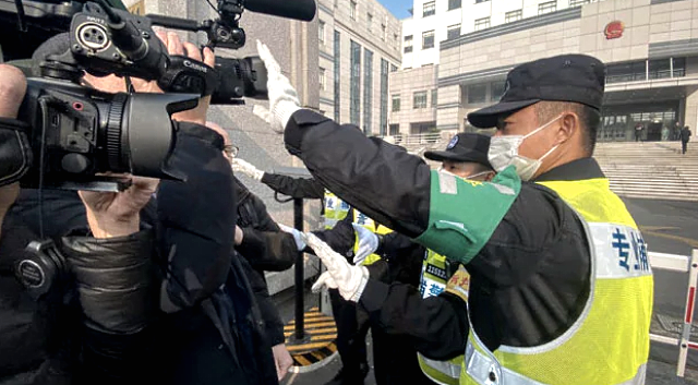 A cop stops journalists from recording footage outside the court where Zhang Zhan is set for trial.