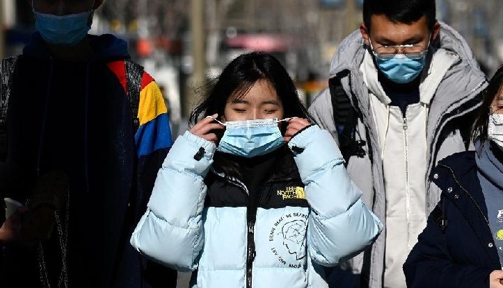 People wearing face masks walk along a street in Beijing on New Year Eve. AFP