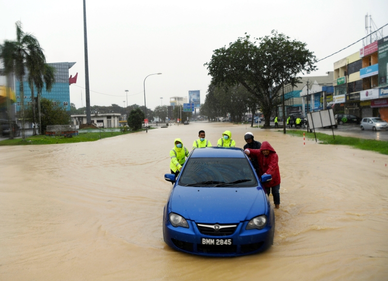 关丹大路变成水城，警察在居民的协助下将一辆滞留在洪水中的汽车推到体育场前。