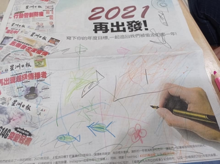 两名小孩在报纸上画上小鱼，充满童趣。