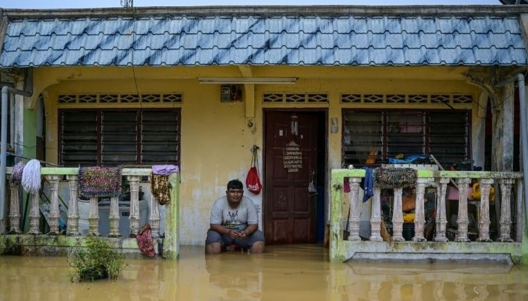 A resident sits outside his home partially submerged in floodwaters in Kuala Kaung near Lanchang, Pahang. AFP