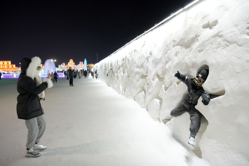 游客在哈尔滨冰雪大世界园区的雪墙边开心留影。（图：新华社）

