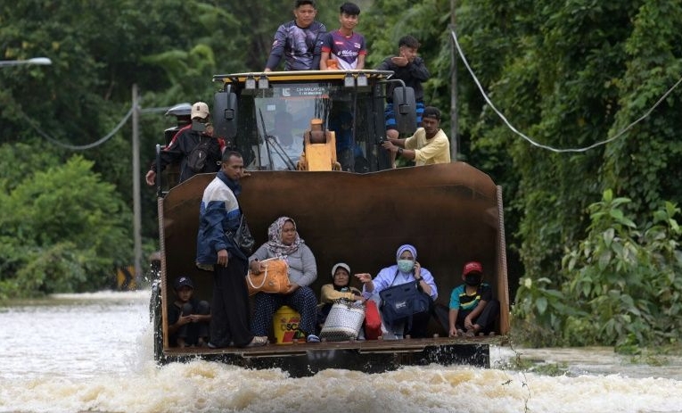 Residents ride a digger through floodwaters following heavy monsoon downpours in Lanchang, Pahang. AFP