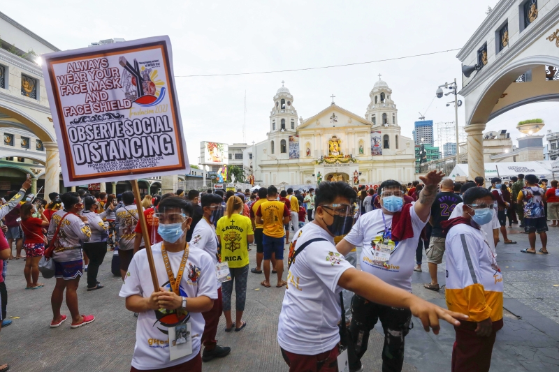 工作人员在马尼拉奎阿坡教堂前高举告示牌，提醒参与弥撒活动的信徒戴口罩及保持社交距离。

