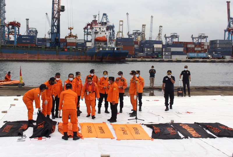 搜救人员将一个个装有死者遗骸的尸袋铺排于港口平台上。（法新社照片）