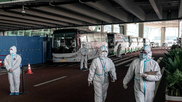 Health workers in personal protection suits stand next to buses at Wuhan airport following the arrival of WHO team. AFP