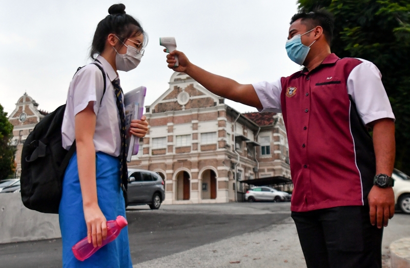 戴著口罩的怡保卫理公会国立中学学生进入校园时，让值勤老师测量体温。