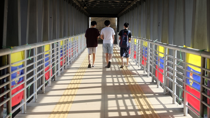 3名年轻人走过挂满直辖区旗帜的行人天桥。

