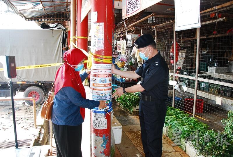 胡昌福（右）和新闻宣传局官员在马口公市柱子上张贴防疫的海报。
