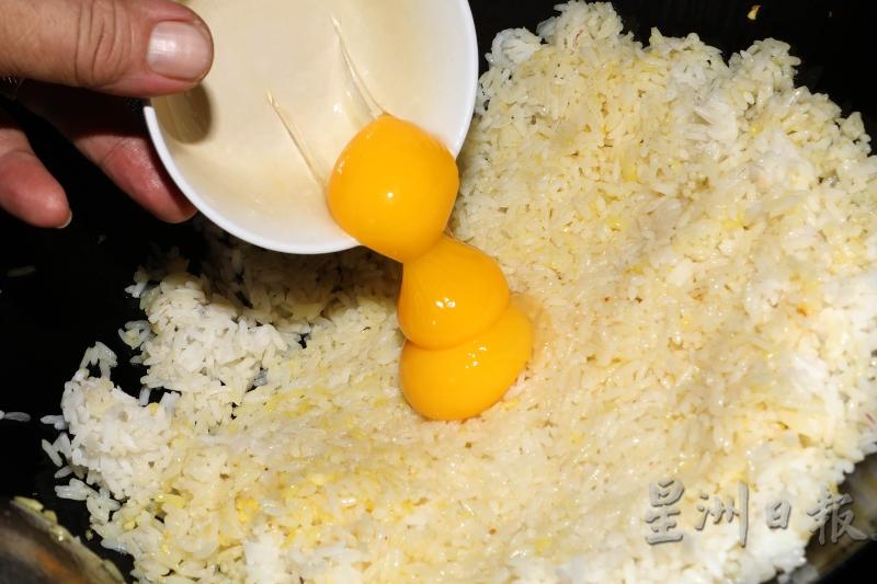 3.把3粒蛋黄倒入饭里兜炒至饭呈现金黄色后，加入虾仁兜炒片刻，加入调味料，盖上焗约1分钟。