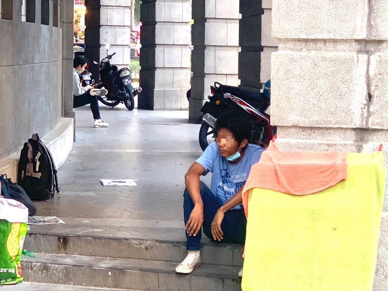 难忍炎热的天气，坐在路旁的街友拉下口罩呼吸。