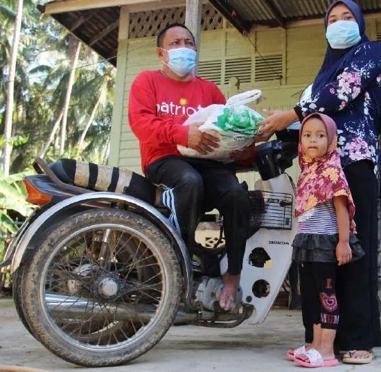 罗斯兰依斯迈（左）骑著三轮摩托车，派发物资给村民。