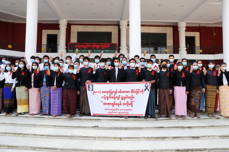 缅甸Yadanabon大学毕业的律师举起三指及横额写着“我们谴责非法政变”的旗帜，表达他们的立场。