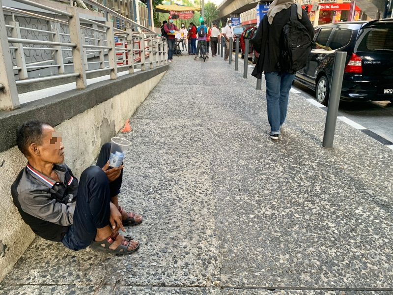 一名街友落寞地坐在路边乞讨。