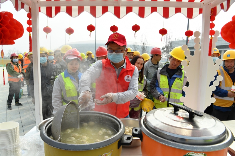 图为志愿者罗皓（红马甲）将煮好的饺子起锅。（中新社照片）　