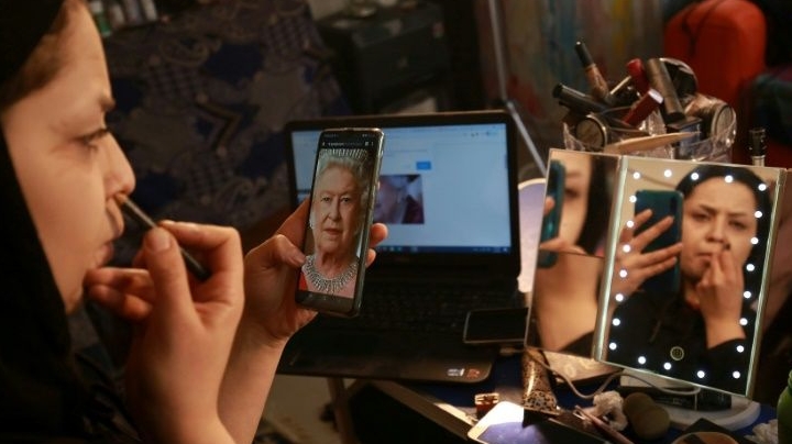 Alaa Bliha uses a portrait of Queen Elizabeth II saved on her mobile telephone to work on her imitation make-up. AFP