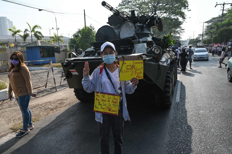 缅甸民众无惧军方应对抗议时越来越多的使用武力，周一继绩上街反对政变。 仰光一名示威者站在装甲车前，举起三指及标语表达反抗决心。（图：法新社）